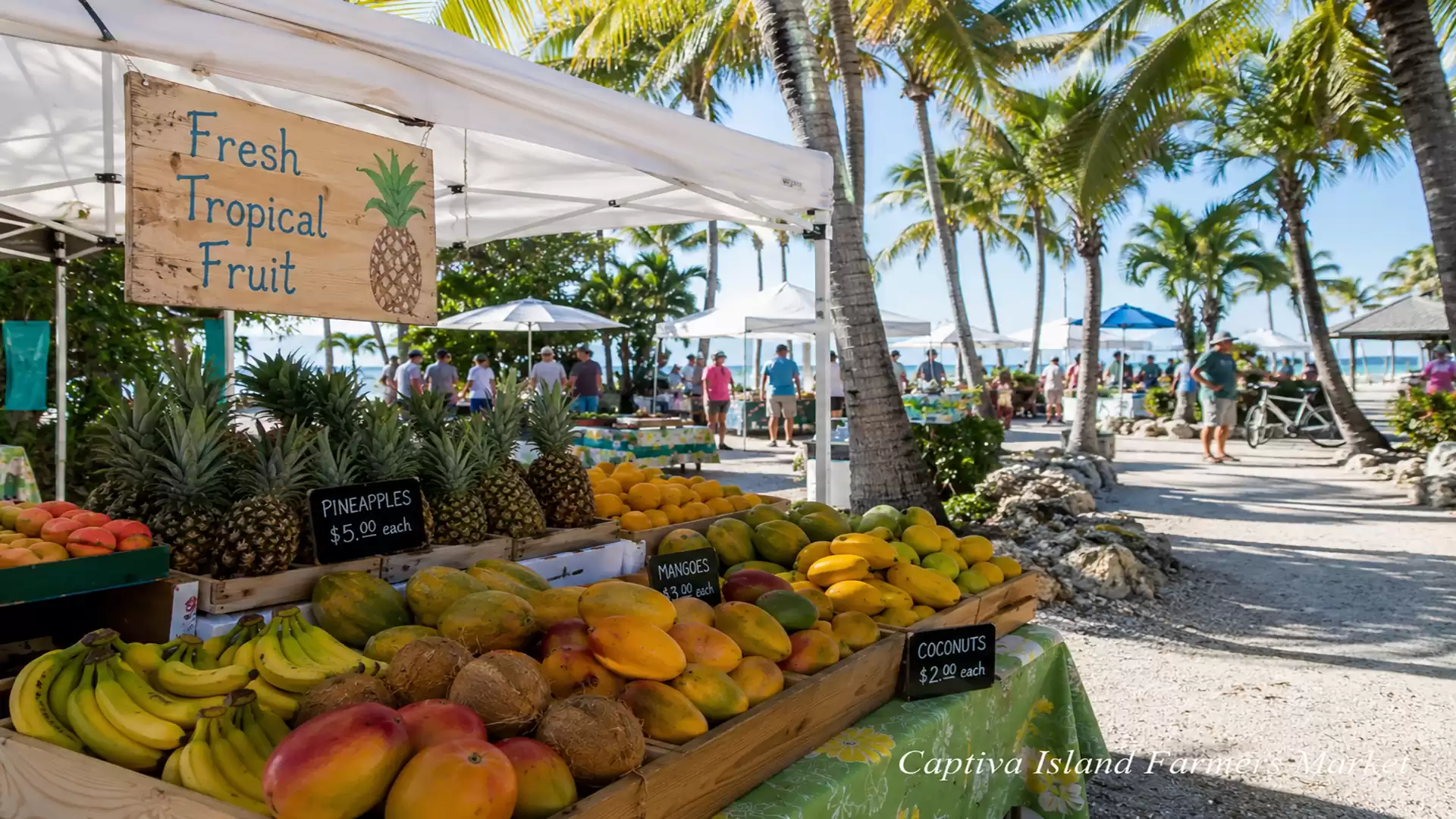 A tropical fruit stand at a market with palm trees in the background. Various fruits like pineapple, mango, and bananas are displayed.
