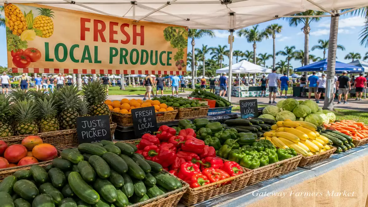 A bustling outdoor farmers' market with colorful fresh fruits and vegetables on a table under a sunshade. Green palm trees and a blue sky are visible in the background.