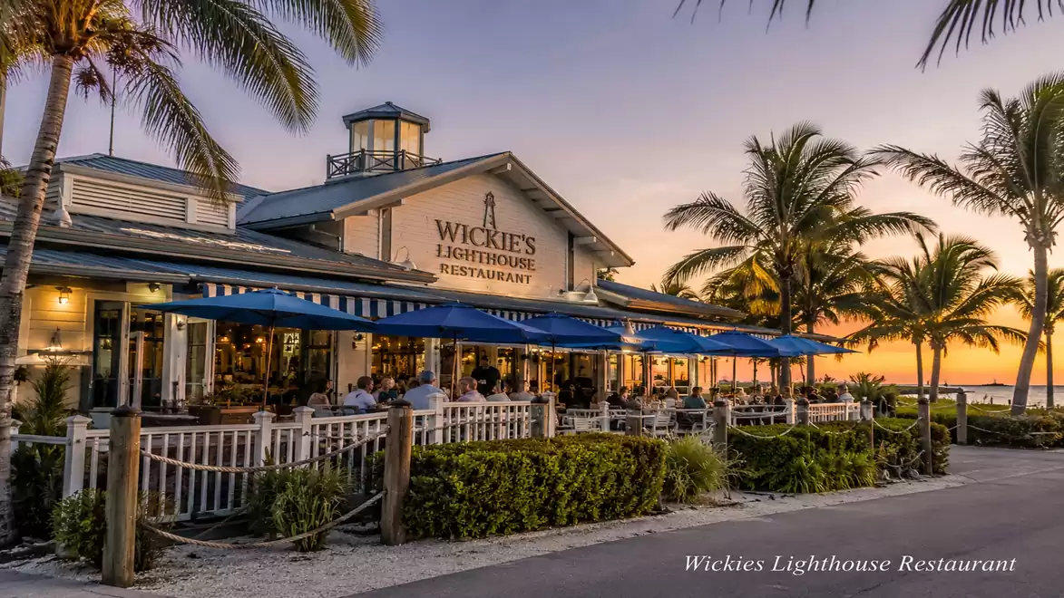 Image of a restaurant at sunset with palm trees and blue sunshades, Wickies Lighthouse Restaurant.