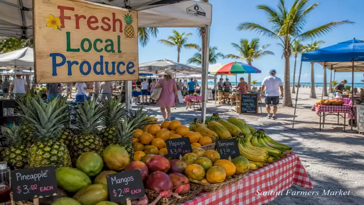 Beachside farmers market with fresh, local produce such as pineapples, mangoes, and bananas on a table with a checkered tablecloth in front of palm trees.