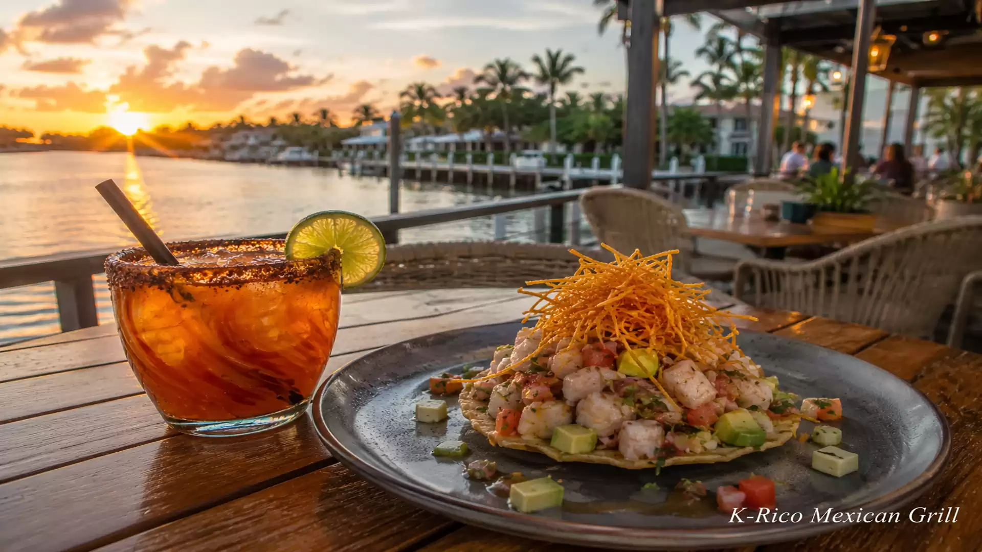 A plate with a Mexican dish and a drink with lime by the water during sunset.
