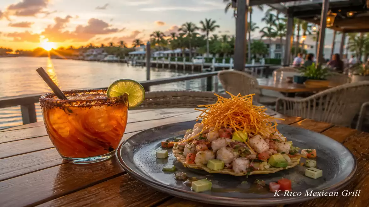 A plate with a Mexican dish and a drink with lime by the water during sunset.