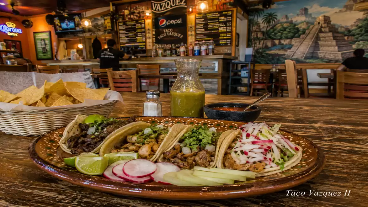 A rustic restaurant with a selection of tacos on a plate. In the background, there's a bar with a painted wall.