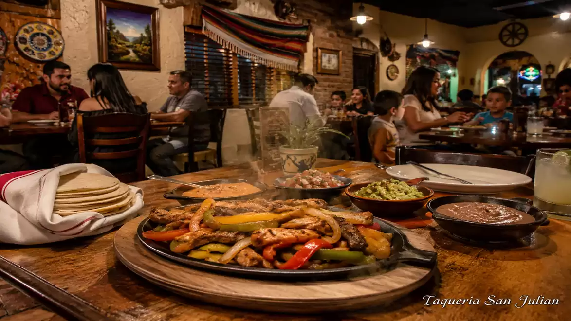 A Mexican restaurant with a table full of colorful dishes and diners in the background in traditional decor.
