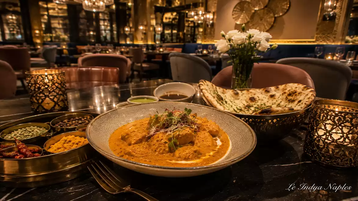 A luxurious Indian restaurant featuring a plate of exotic curry dishes, naan bread, and elegant interior decor.