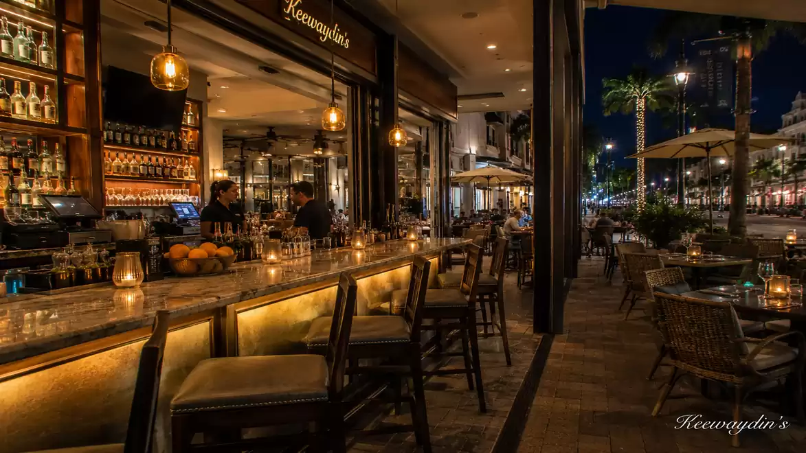 A cozy outdoor bar area at night with orange lighting, seating, and an illuminated counter.