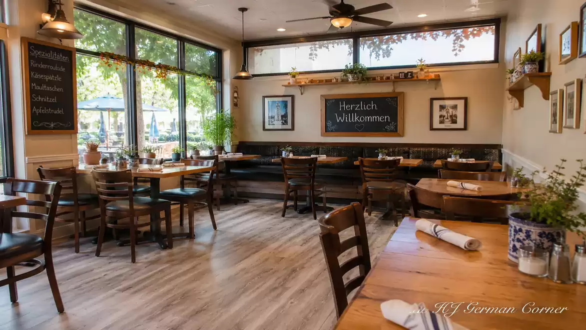 A cozy German restaurant with wooden tables, chairs, and a 'Welcome' sign. Large windows allow plenty of light.