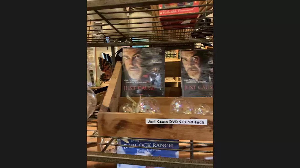 A wooden shelf with DVDs of the movie 'Just Cause' and a sign indicating each DVD costs $12.50.