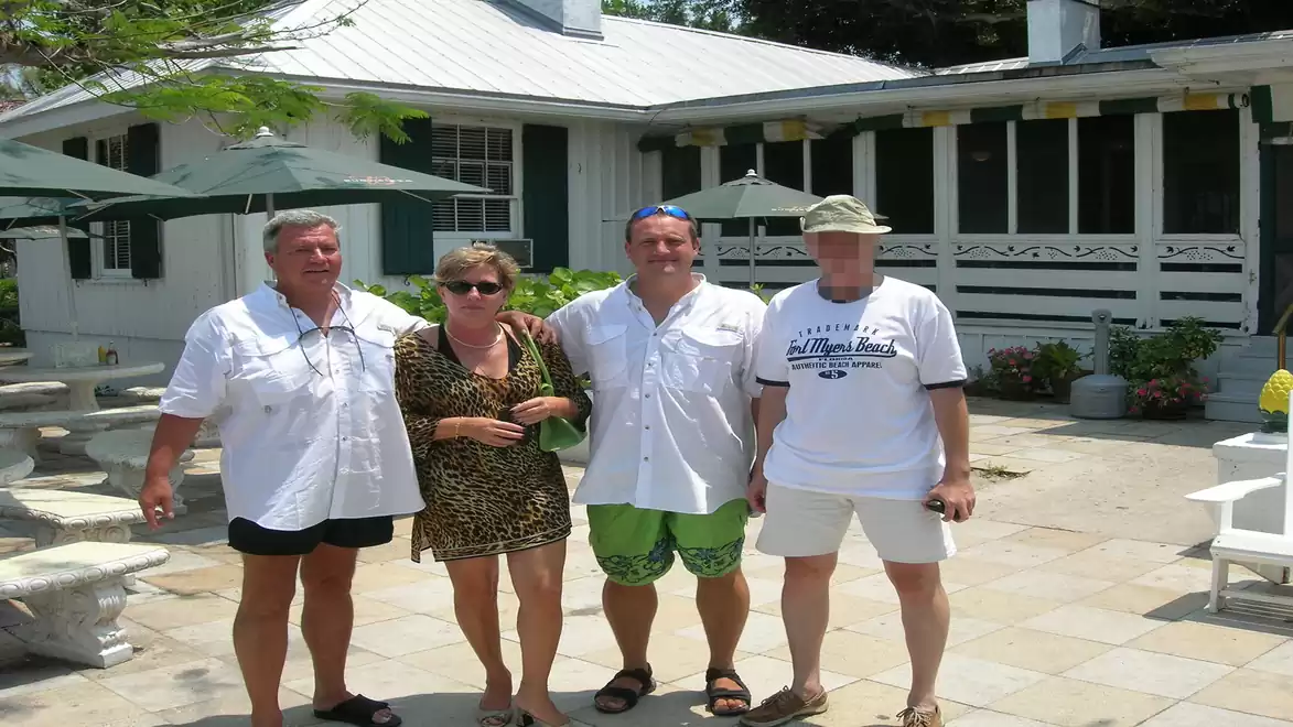 Four people standing together outside a white building with umbrellas and plants.