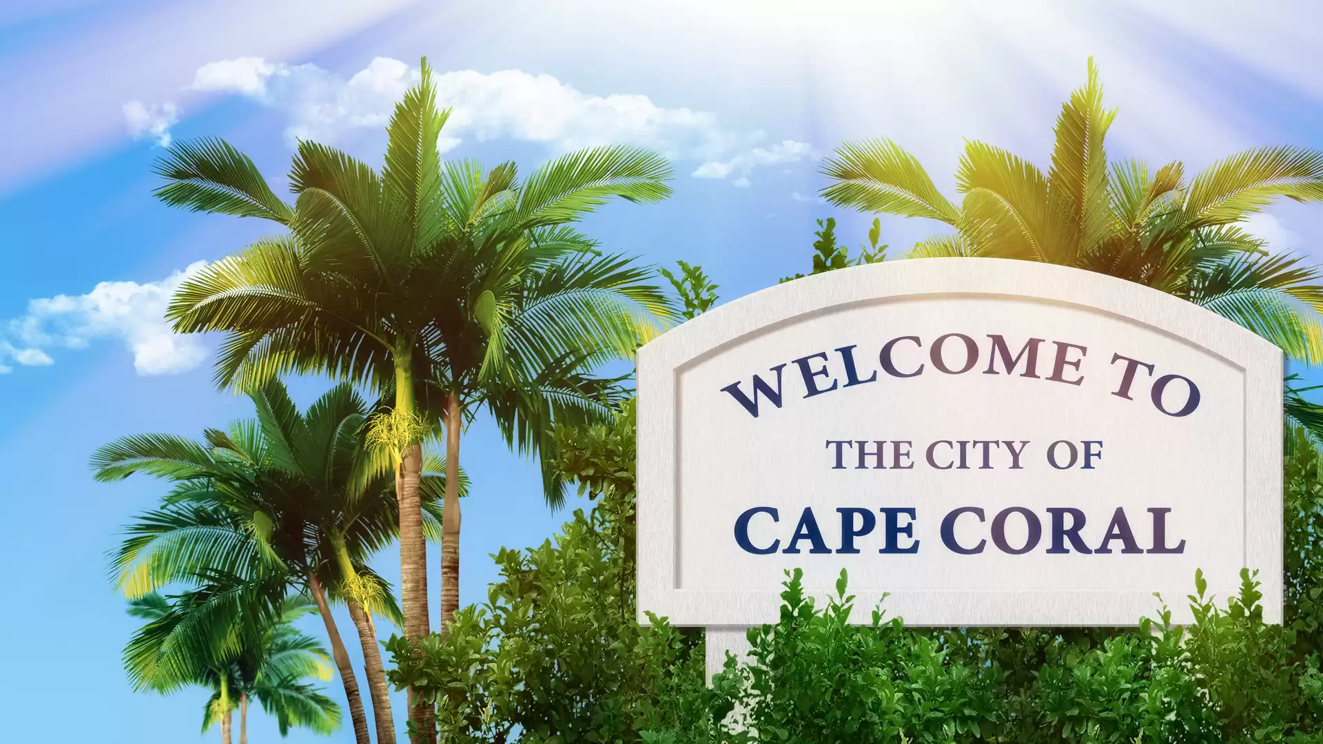 Welcome sign of Cape Coral city with palm trees in the background under a blue sky.