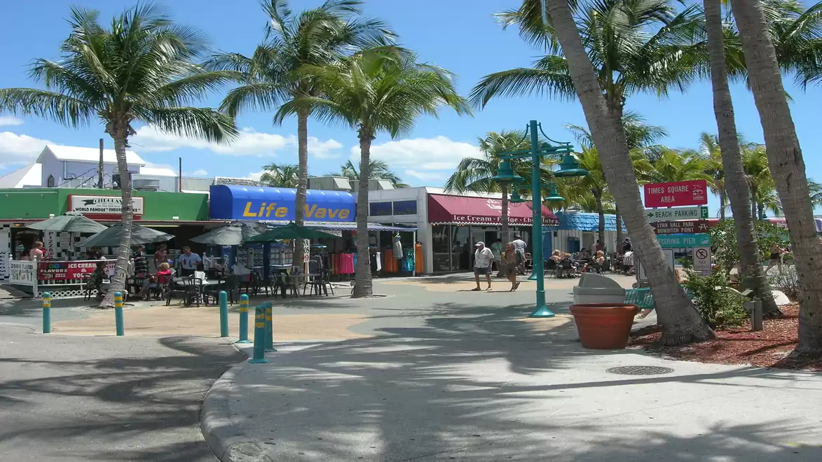A lively marketplace with palm trees, various shops, and people strolling along the stores.