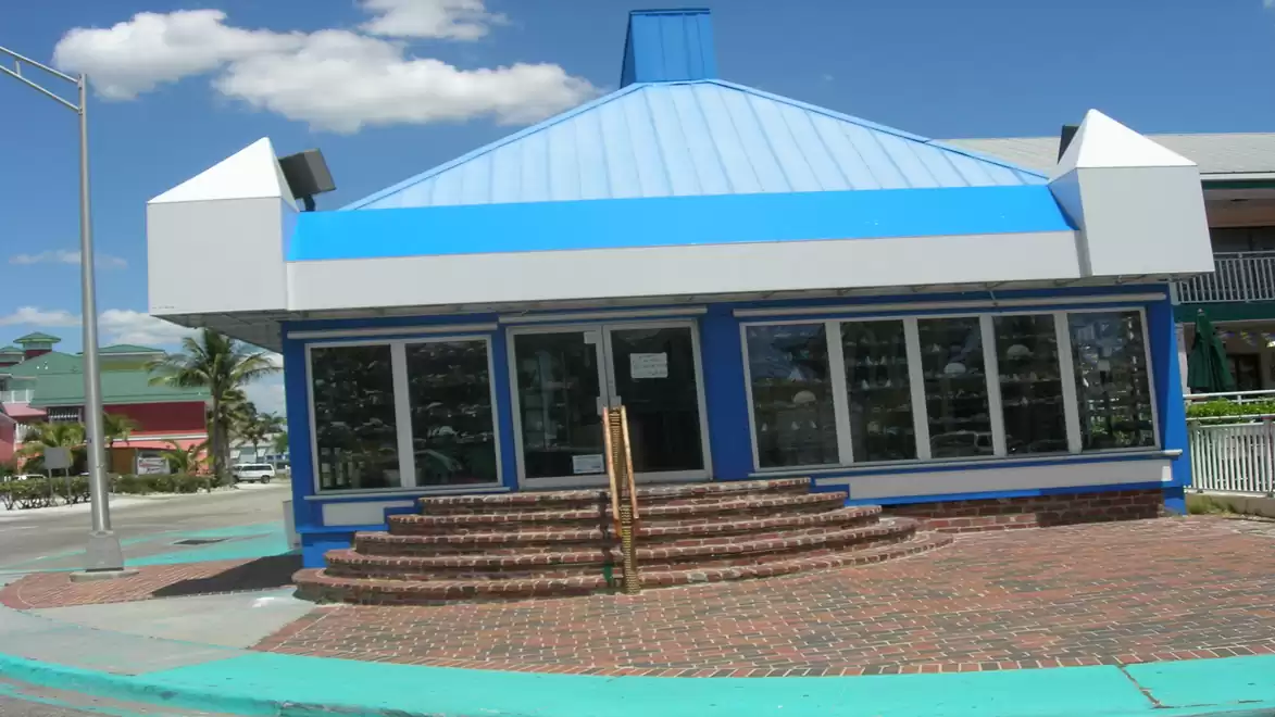An abandoned blue and white-painted building with stairs and large windows under a clear sky with clouds.