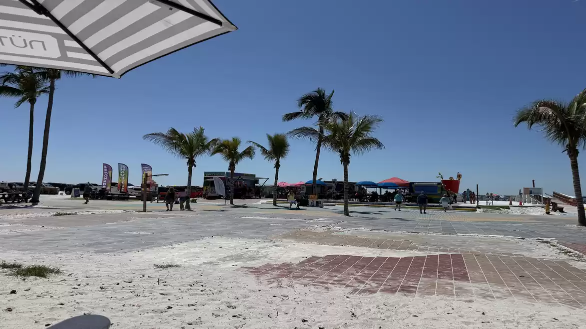Beach promenade with palm trees, umbrella, and blue sky.