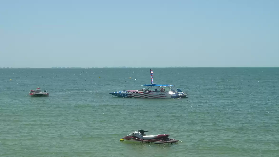 Three boats in a calm sea on a sunny day, including a large boat in the background with an American flag.