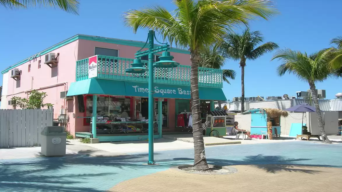 A colorful Caribbean-style bar with a turquoise roof and pink facade, surrounded by palm trees in a sunny setting.