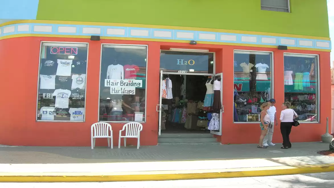 Colorful store with an orange facade and green top. Display windows show clothing and a sign for hair braiding. Two chairs are in front of the shop.