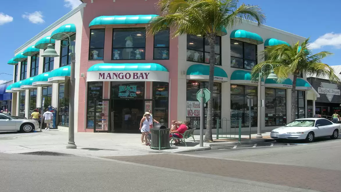 Corner shop with turquoise awnings and palm trees at a sunny street corner, labeled 'Mango Bay'.