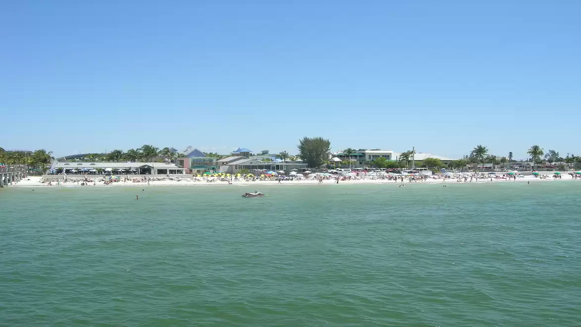 A lively sandy beach on a clear, sunny day with blue skies and numerous people enjoying the beach scenery.
