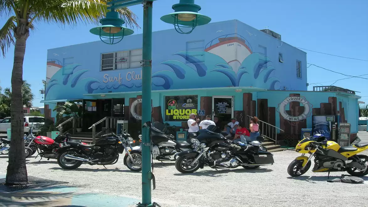 Motorcycles parked in front of a colorful store with a blue facade and beach mural, under a clear blue sky.