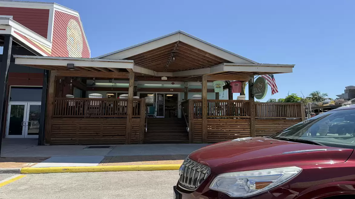 Exterior view of a restaurant with wooden porch and US flag under clear blue sky, with a red car in the foreground.