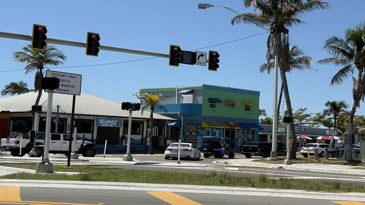 Street scene with traffic lights, palm trees, and colorful buildings at an intersection on a sunny day.