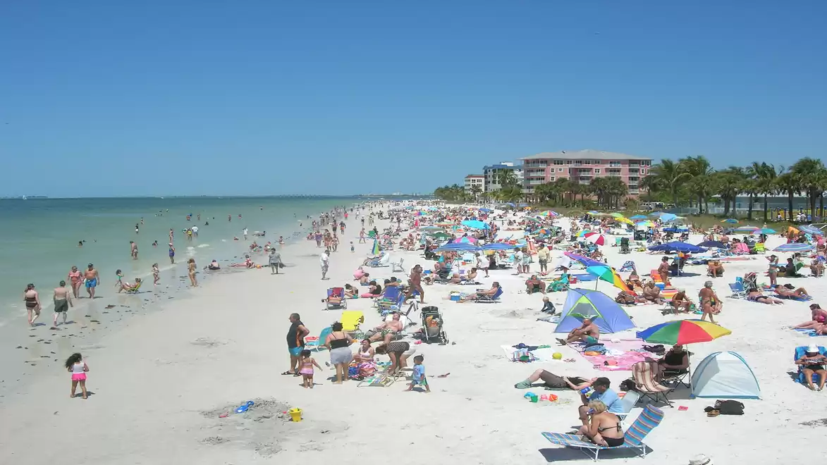 On a sunny beach day, numerous people relax under colorful umbrellas, swim in the clear water, and enjoy the summer atmosphere.