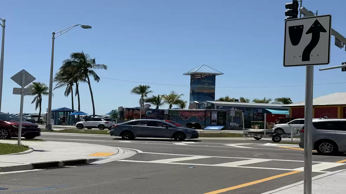 Intersection in a tropical setting with palm trees, traffic signs, and vehicles under sunny weather.