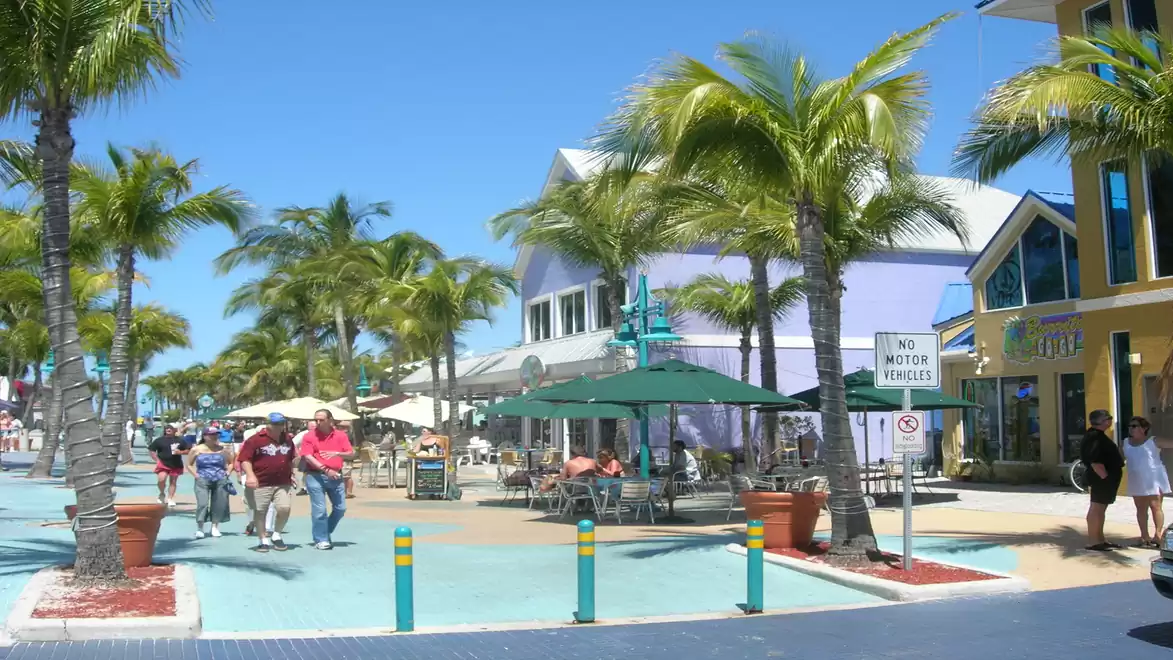 Street scene in a tropical city with palm trees, colorful buildings, and pedestrians in bright sunlight.