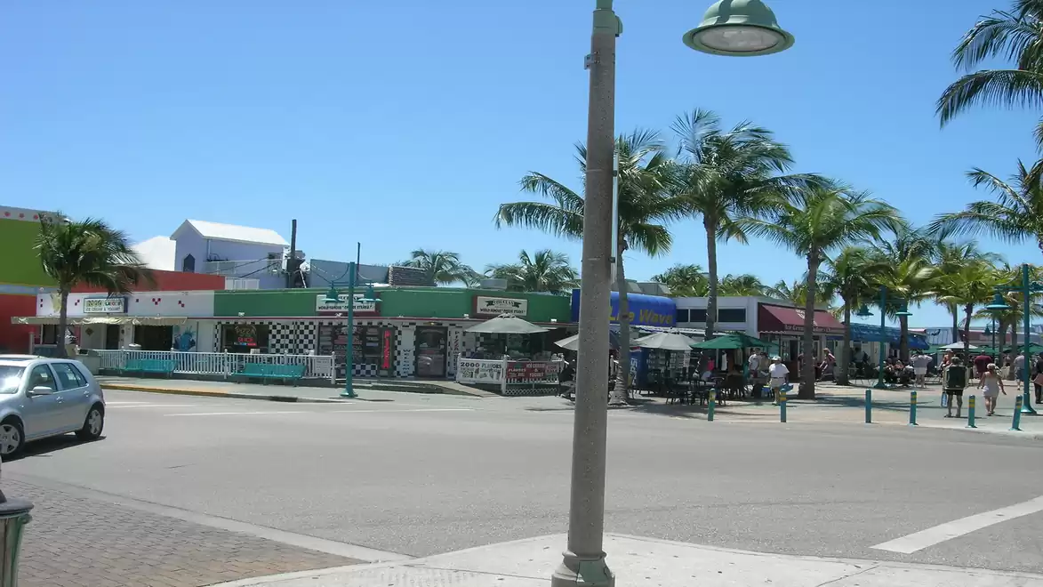 Urban scene with a street lined by colorful shops and palm trees under a clear sky.
