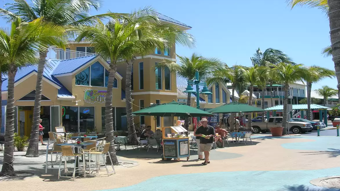 A vibrant street café area with palm trees and blue umbrellas on a sunny day.