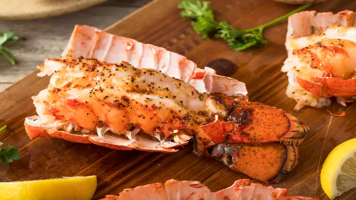 Baked lobster tails served on a wooden board, garnished with lemon slices and parsley.
