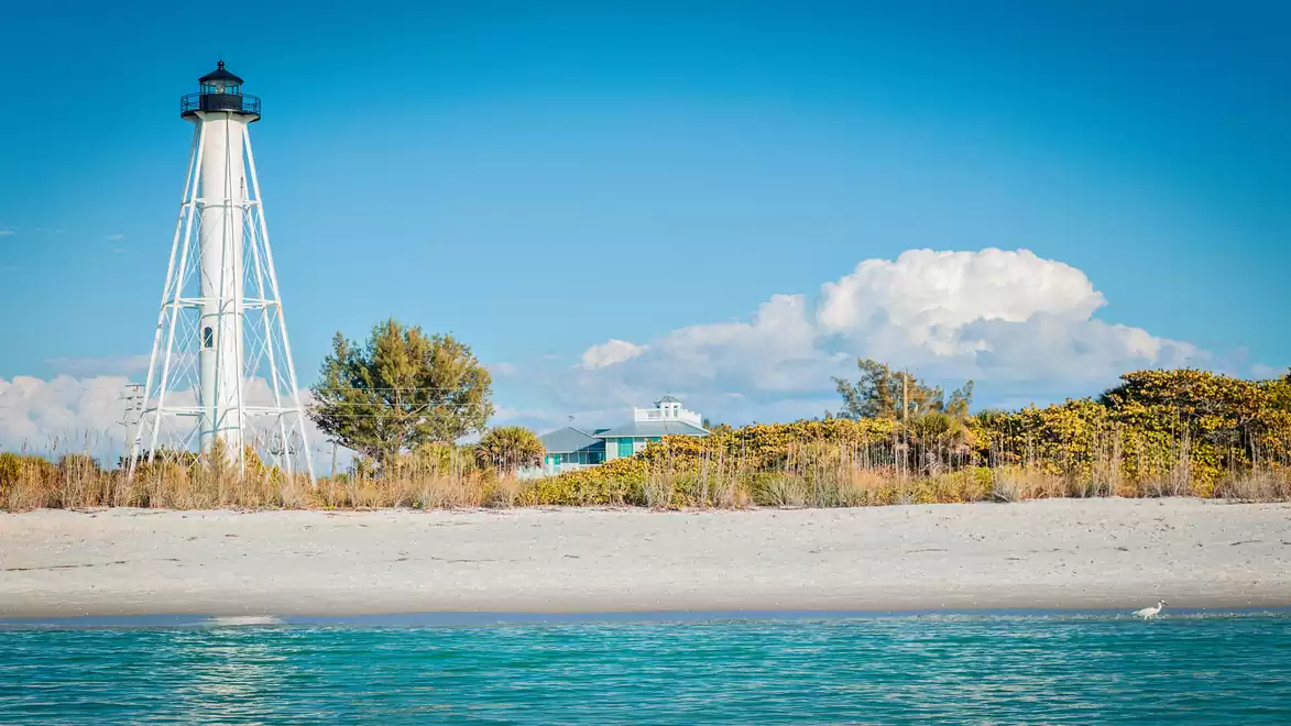 A lighthouse on a sunny beach with a clear blue sky and calm sea.