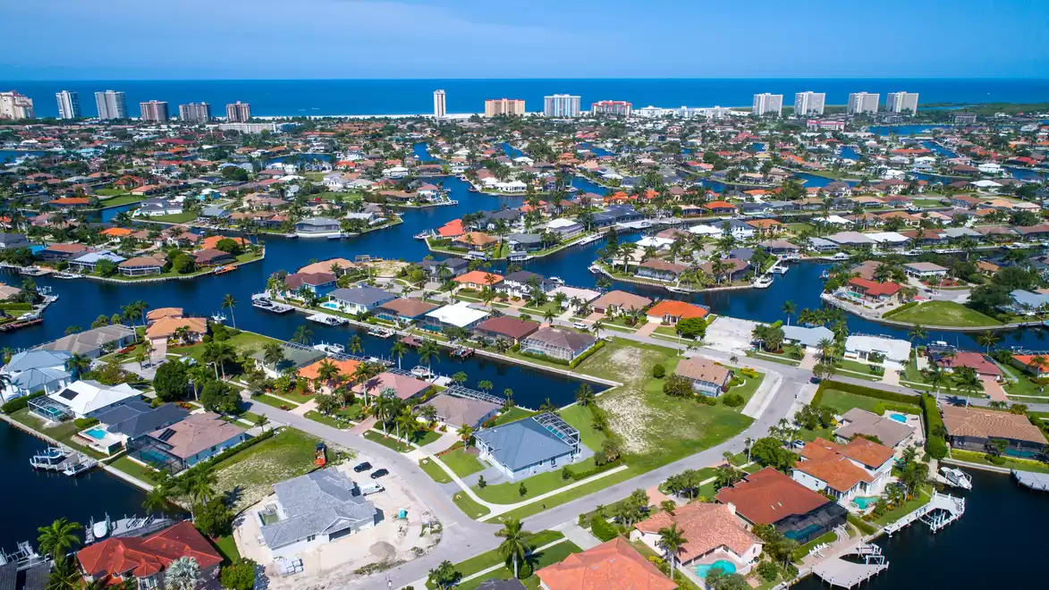 Aerial view of a coastal city with numerous canals and colorful houses, with the blue sea in the background.