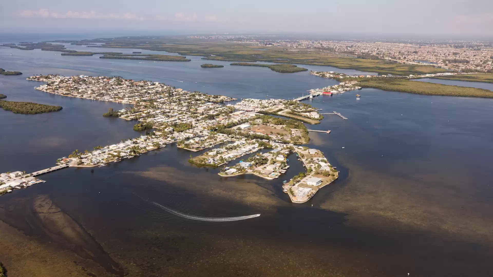 Aerial view of a coastal city with multiple islands and waterways, surrounded by blue water and distant horizon.