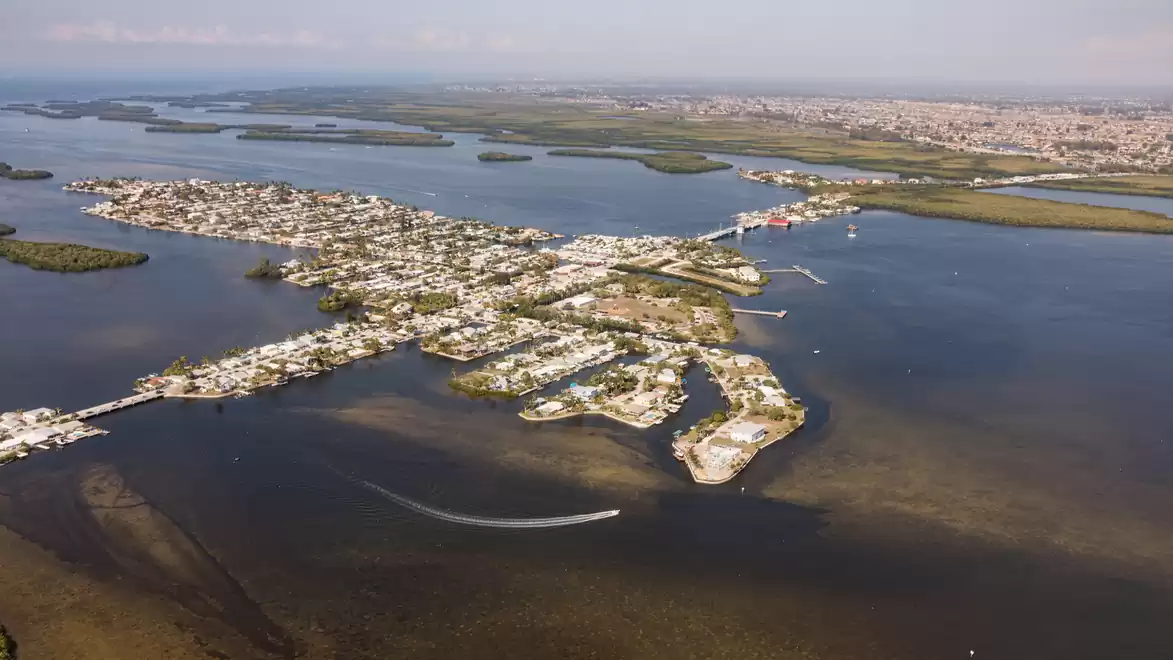 Aerial view of a coastal city with multiple islands and waterways, surrounded by blue water and distant horizon.