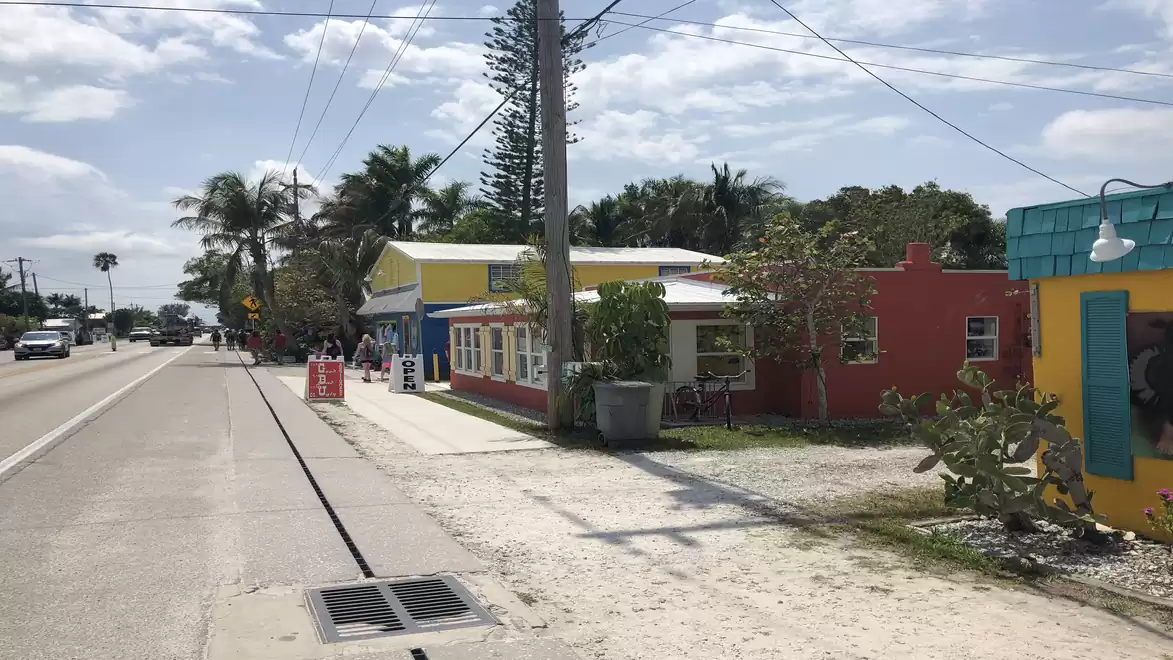 Colorful houses and palm trees along a sunny road leading into the distance.