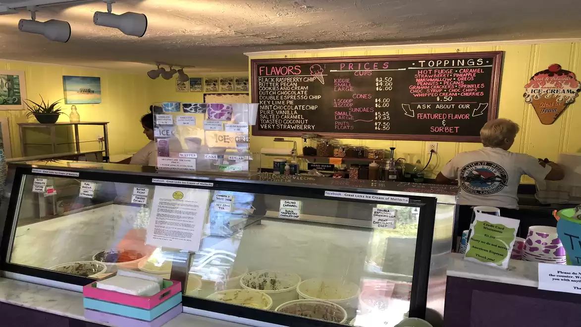 Interior view of an ice cream shop with a variety of flavors and toppings listed on a board.