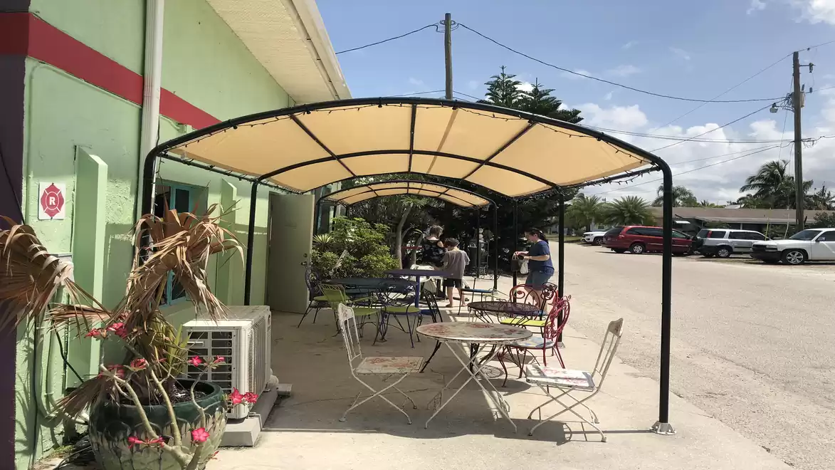 An outdoor area of a café with sunshade and empty tables and chairs by a street.