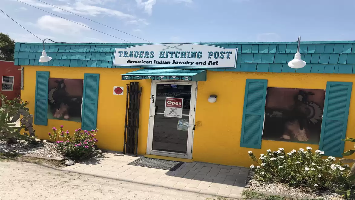 A small yellow building with turquoise shutters and a sign saying 'Traders Hitching Post'. It sells American Indian jewelry and art.