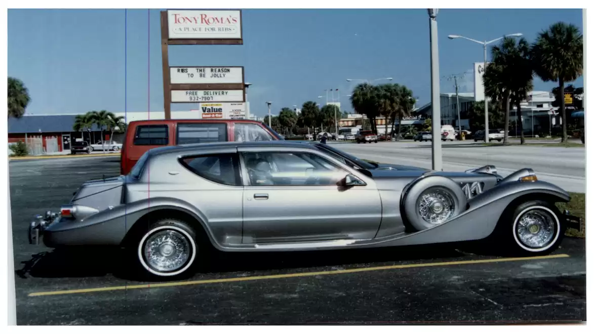 A silver, classic-inspired vehicle with a unique design parked in a lot in front of a business complex on a sunny day.