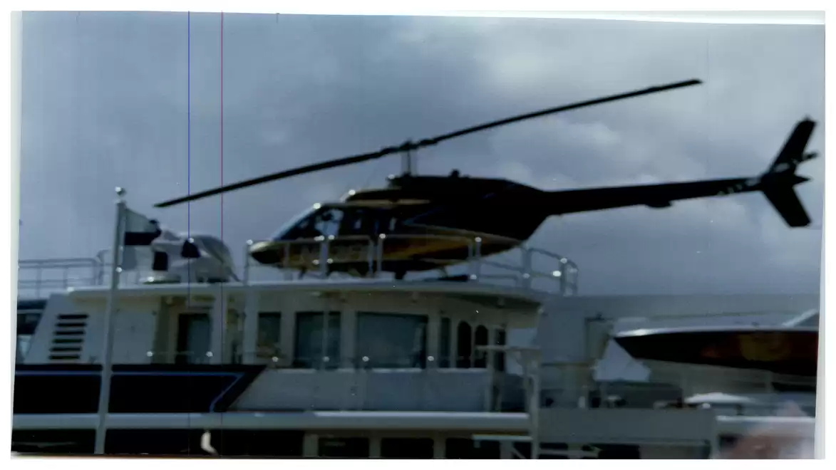 A helicopter landing on the platform of a large ship under a cloudy sky.