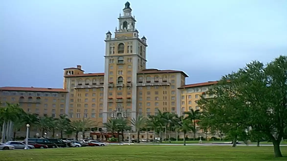 Historic, multi-story building with a tower top, surrounded by palm trees.