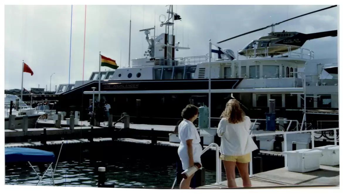 Two people standing at a modern marina with a large yacht in the background.