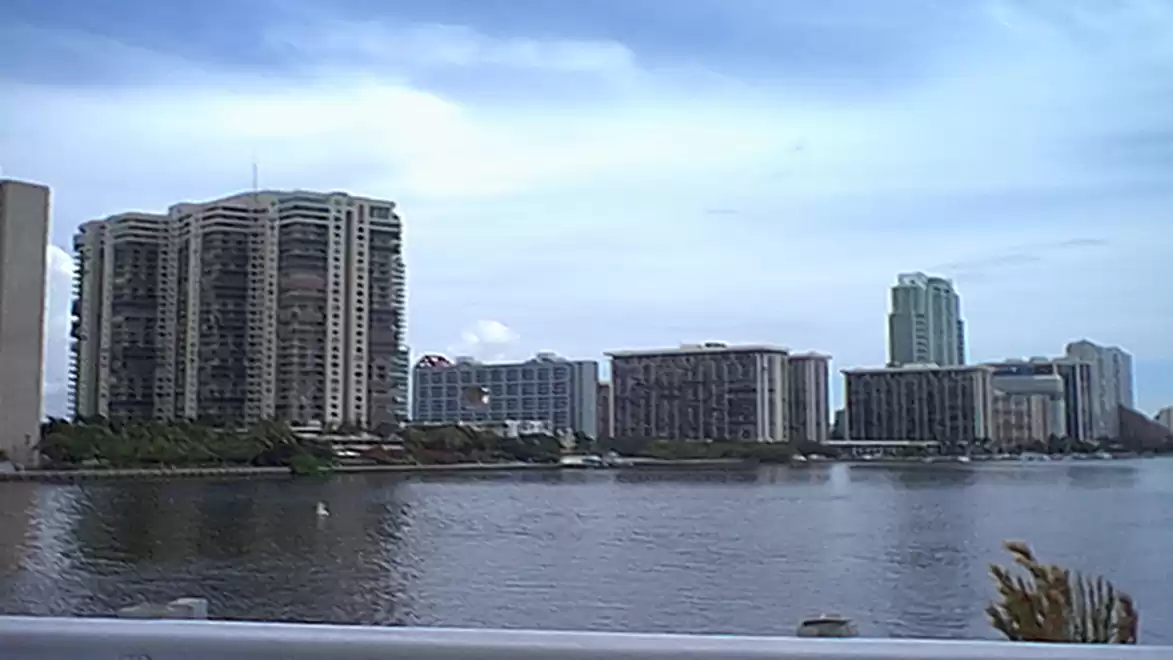 Panoramic view of a modern skyline with tall buildings by the water under a cloudy sky.