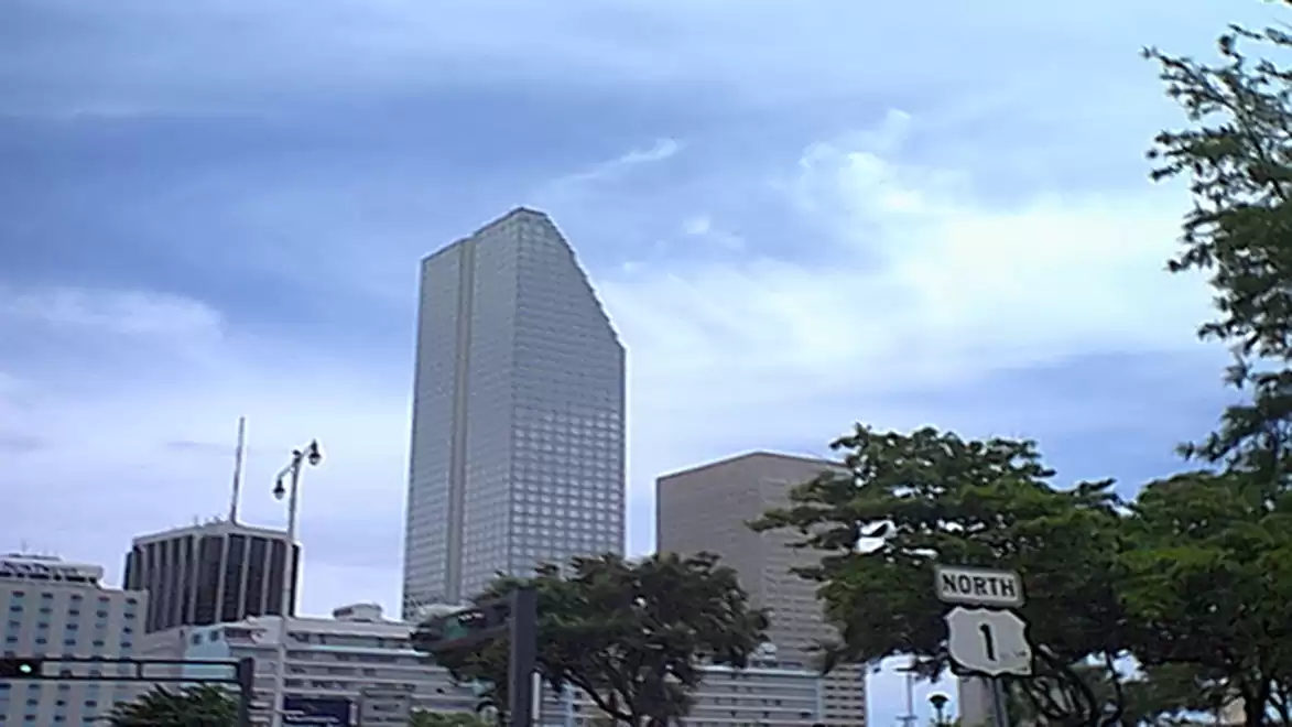 Urban skyline with tall skyscrapers, including a prominent glass high-rise building under a cloudy sky.