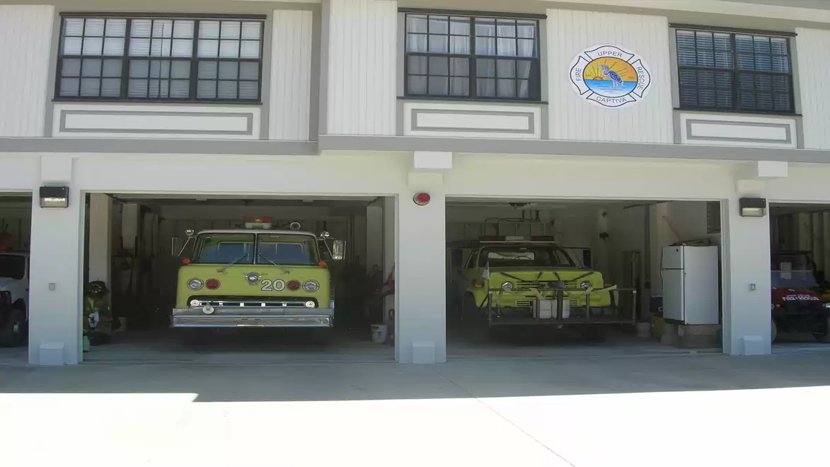 A fire station with two yellow fire trucks in open garages. Above are windows and a round logo on the wall.