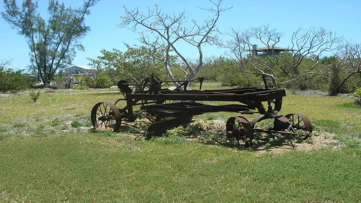 An outdated agricultural plow lies on a grassy field under a clear blue sky.