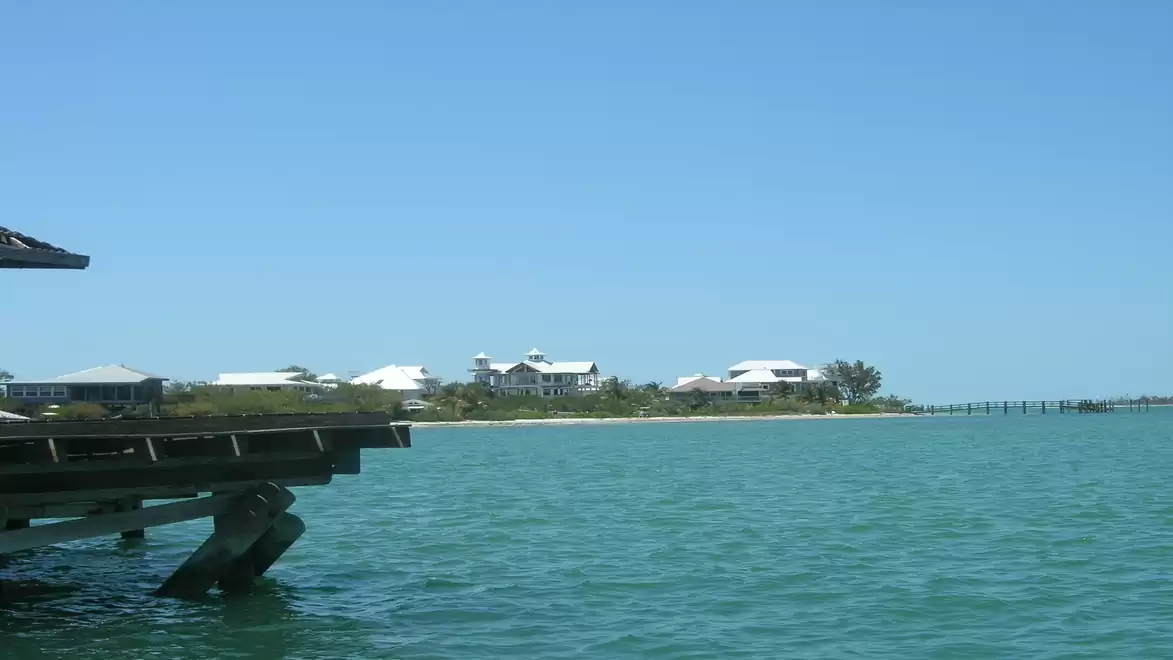Panoramic view of a coastal area with blue water, wooden dock, and buildings in the background on a sunny day.