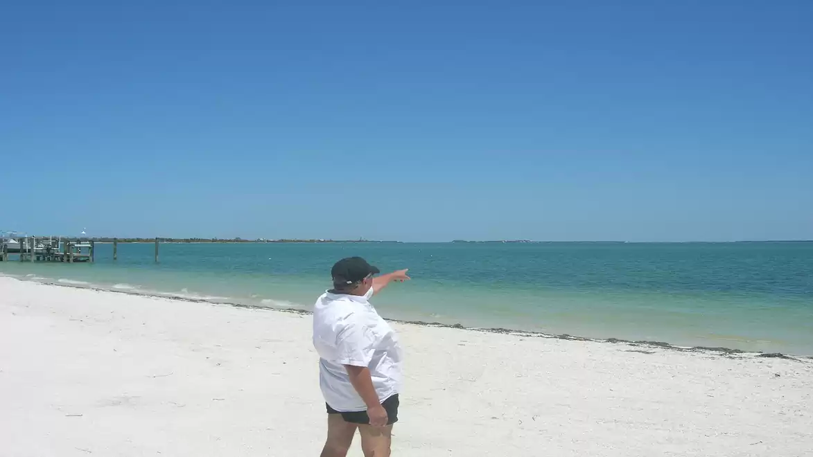 Person on the beach pointing at the sea under a clear blue sky.
