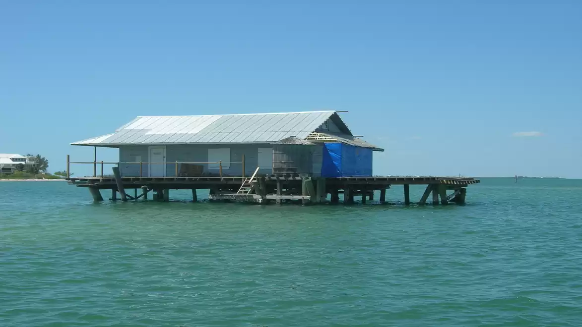 A stilt house in the sea with a blue sky in the background.